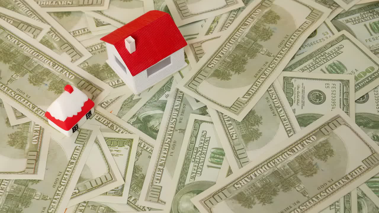 A small miniature model house placed on scattered stack of dollar bills banknotes represents real estate investment opportunities, home ownership, and the financial aspects of buying a property