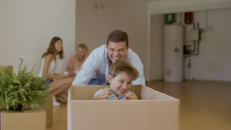 Vater-Schiebt-Sohn,-Der-In-Kiste-Sitzt,-Nach-Dem-Umzug-Durch-Das-Haus