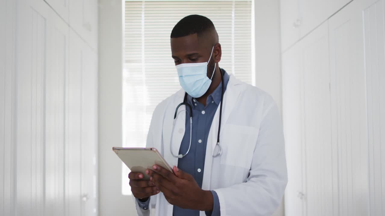 African american doctor wearing face mask using digital tablet at home