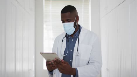 African-american-doctor-wearing-face-mask-using-digital-tablet-at-home