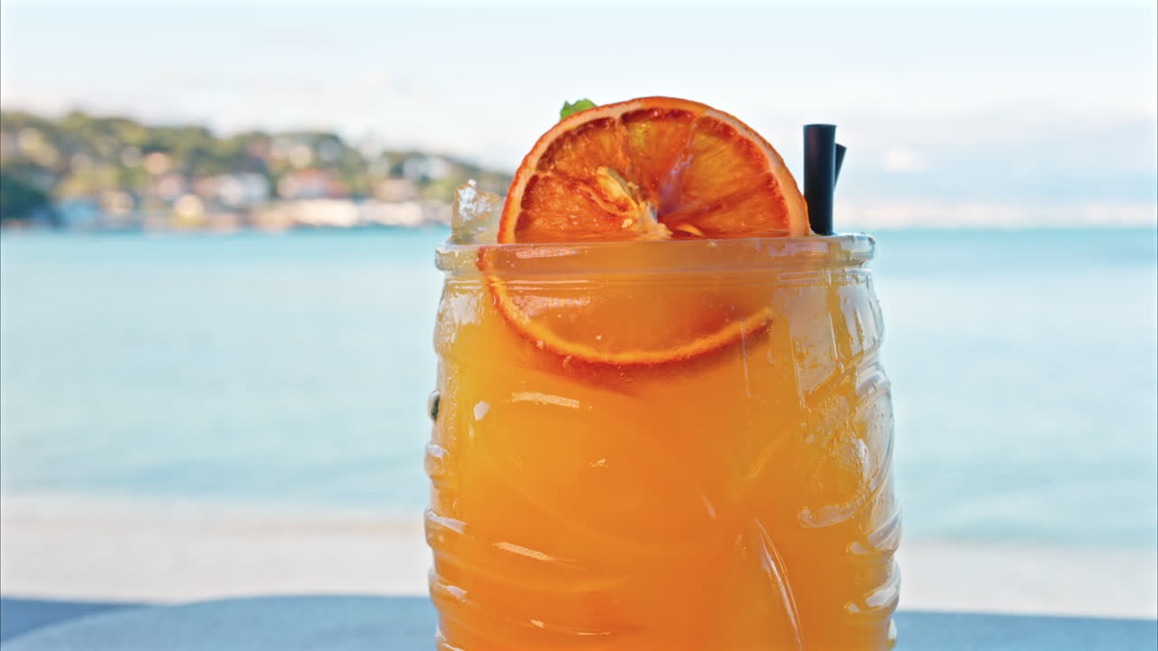 Close up of an orange cocktail on a table with a blurred view of the sea on the background