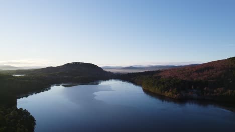 Aerial-drone-footage-flying-high-above-the-surface-of-still-water-with-reflections-in-the-Cairngorms-National-Park,-Scotland-with-a-native-forest-and-mountain-landscape-at-sunset