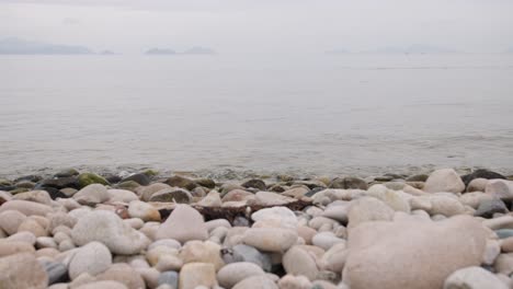 waves gently wash over round rocks at a hazy beach in south korea.