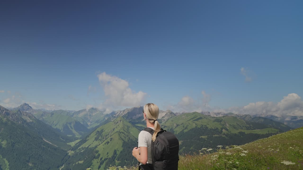 A woman hikes through the scenic Austrian Alps, taking in mountain views under a bright sky