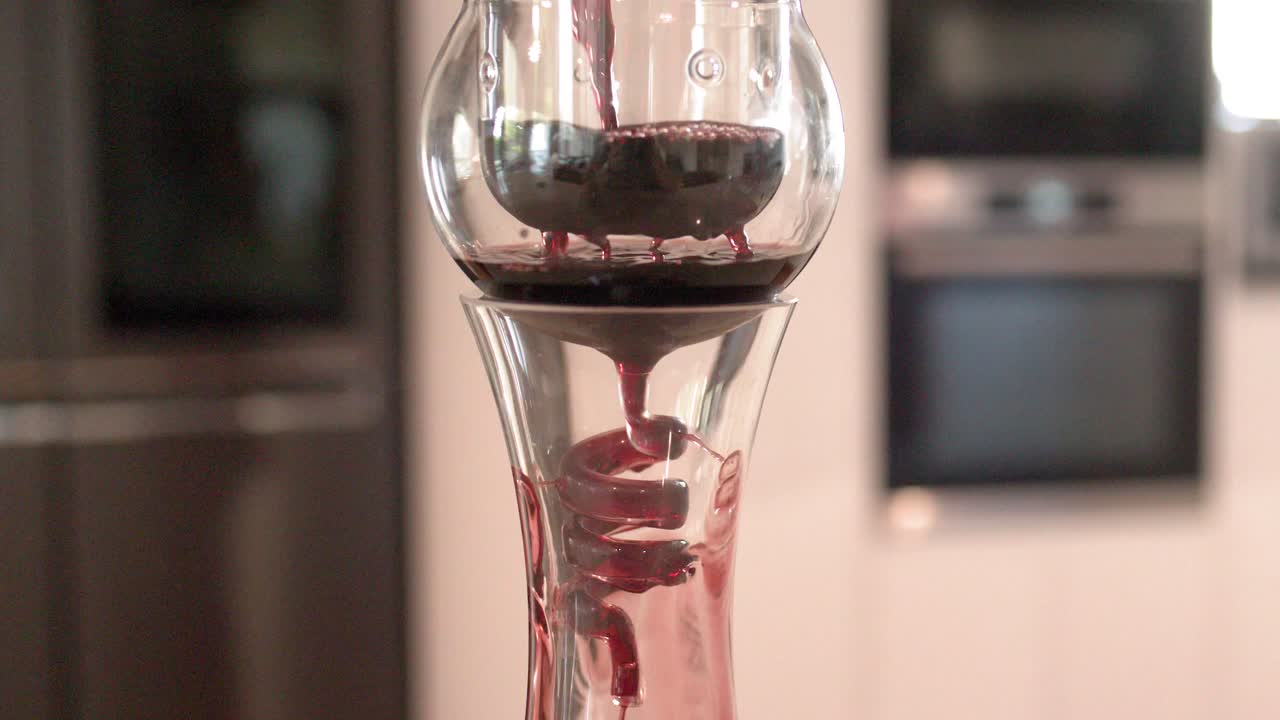 Vino tinto fluye a través de un aireador de cristal a un decantador en una cocina moderna.