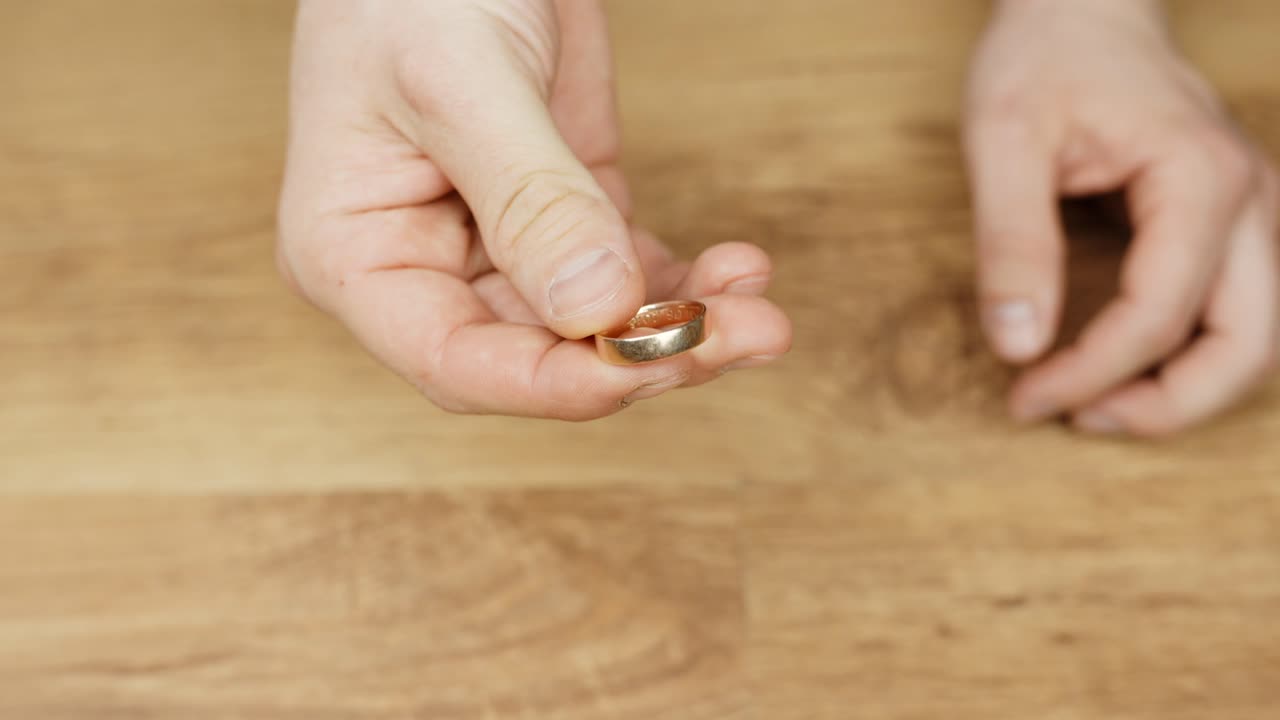 Close-up of hand holding a gold ring on wooden surface, calm and focused moment