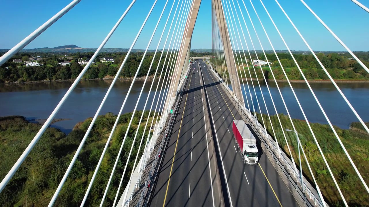 Drone bergerak di sepanjang jembatan gantung di antara kabel dengan lalu lintas mengalir di bawah di atas sungai di Waterford, Irlandia pada hari musim panas.