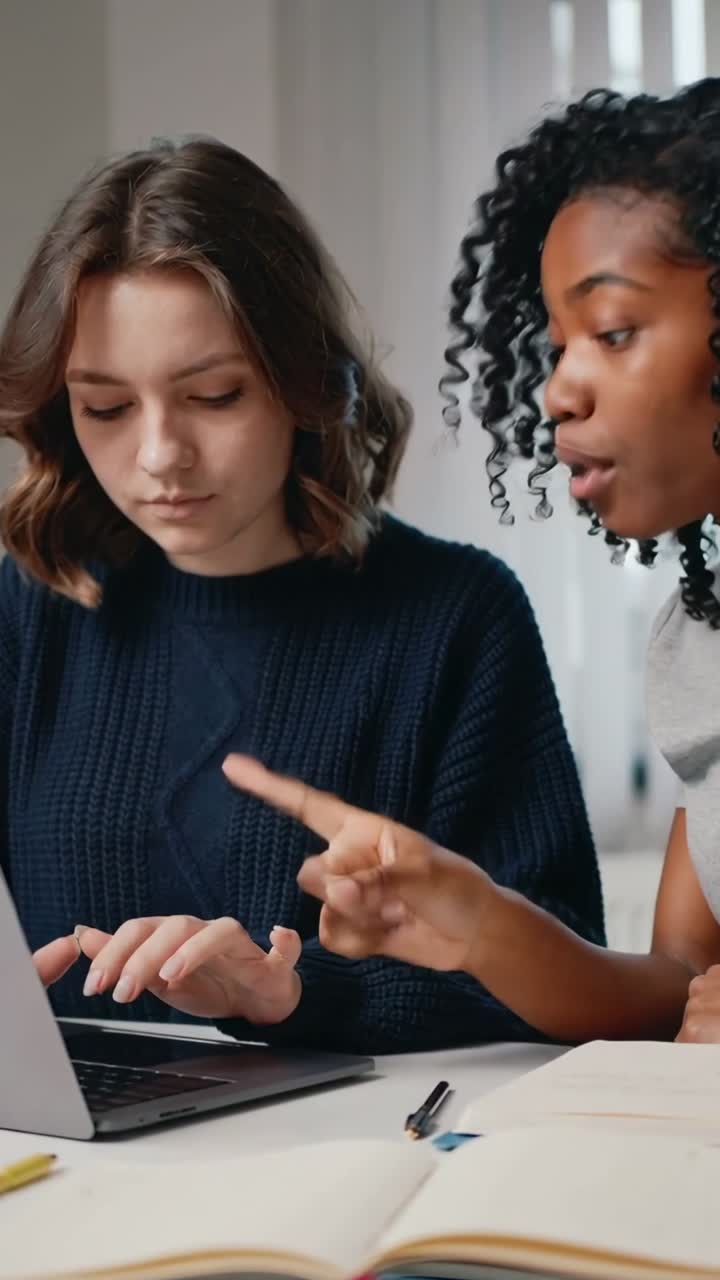 Video verticale: Indicando a destra, collega che guida a sinistra con maglione blu navy che digita su un laptop con appunti al tavolo.