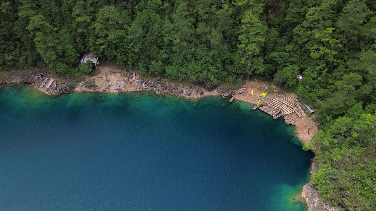Ripresa aerea statica dall'alto con drone di una sponda di lago turchese con pontili in legno e fitta pineta ai Laghi di Montebello, Chiapas, Messico.