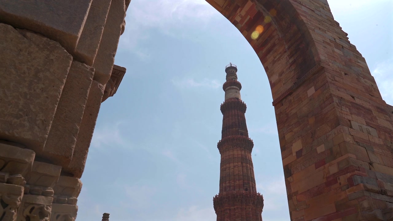 Frøperspektiv af den historiske Qutub Minar røde sandstensminaret indrammet af gamle stenruiner ved Qutb-komplekset i New Delhi, Indien