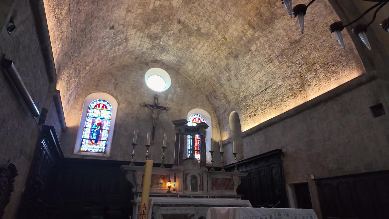 Interior of Collégiale de la Conversion de Saint Paul in Saint Paul de Vence, featuring a stone vaulted ceiling, altar, stained glass, and intimate medieval church setting.