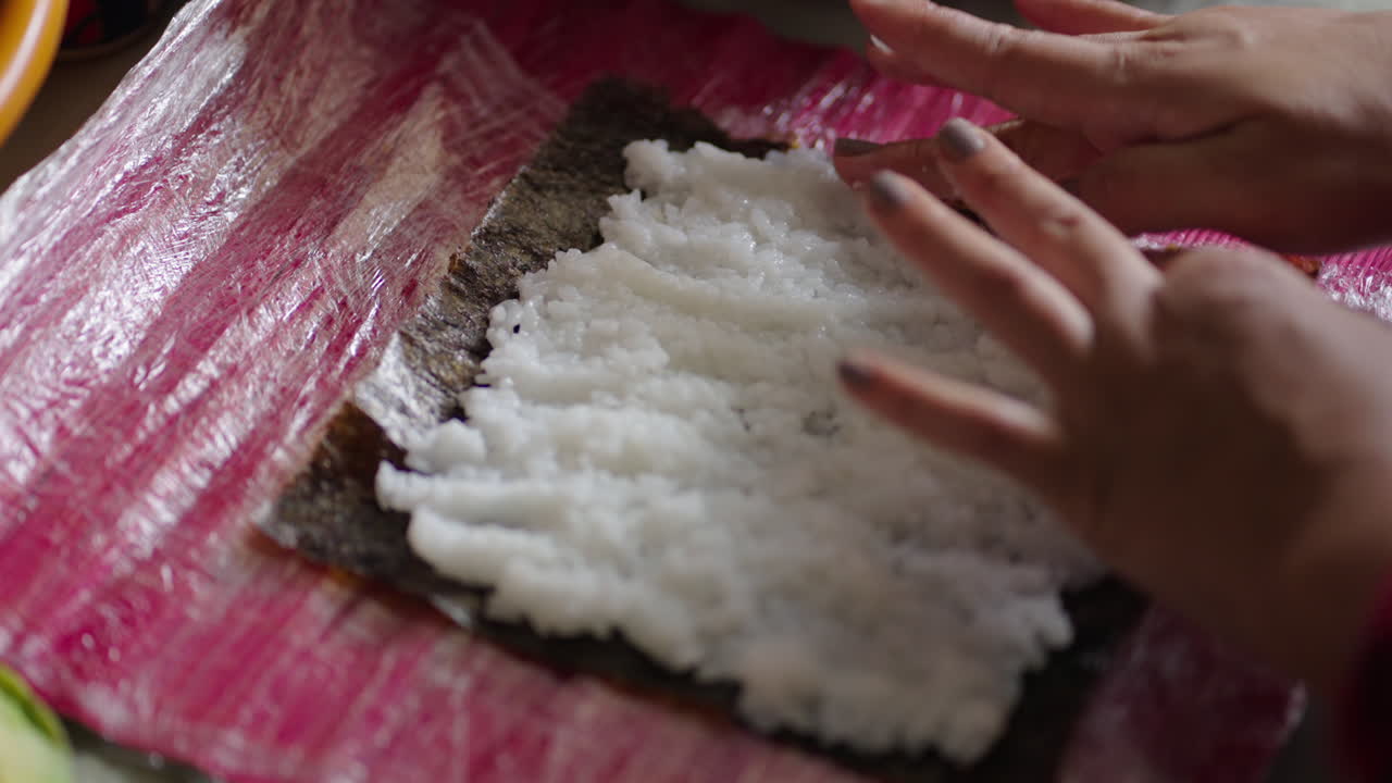 Chef hands gently spread warm shari sushi rice over a nori seaweed sheet on a bamboo makisu mat, using precise sushi‑zaiku technique to prepare makizushi rolls with layer before filling and rolling