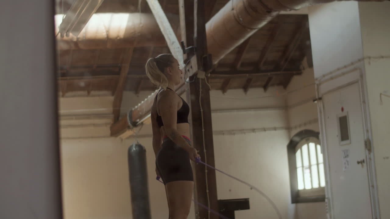 Vista laterale di donna atletica che salta la corda in sala allenamento