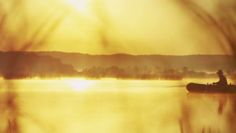 distant view of an old man with a hat on a boat fishing with a rod on the lake on a cloudy morning