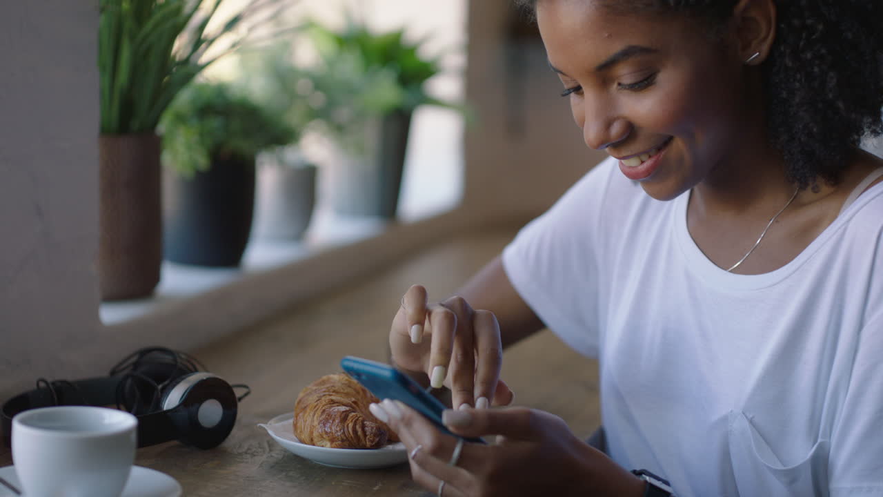 mujer afroamericana feliz usando un teléfono inteligente en un café navegando por mensajes en línea bebiendo café mujer negra enviando mensajes de texto compartiendo estilo de vida en las redes sociales disfrutando del teléfono móvil