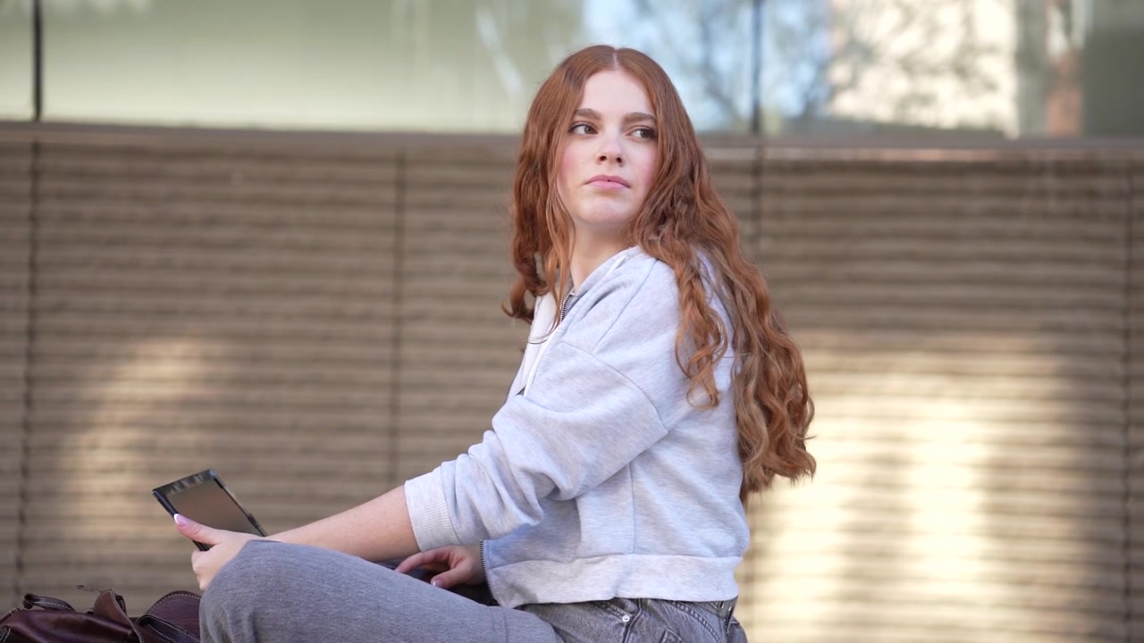 Una giovane donna casual si rilassa in un contesto urbano, con lo smartphone in mano.
