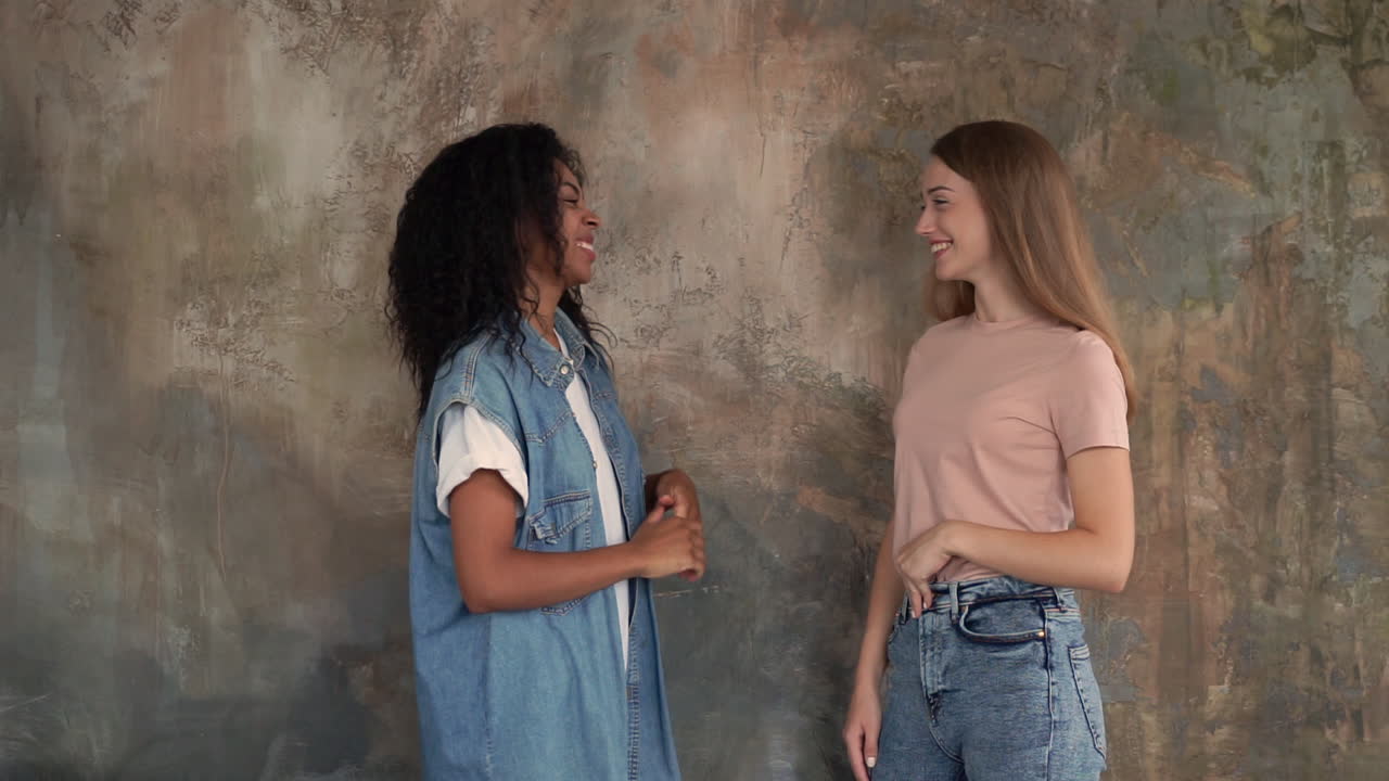 Black girl and caucasian young woman talk and laugh. Two female friends high five. Medium shot.
