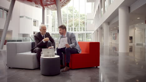 two businessmen discuss document in lobby of modern office