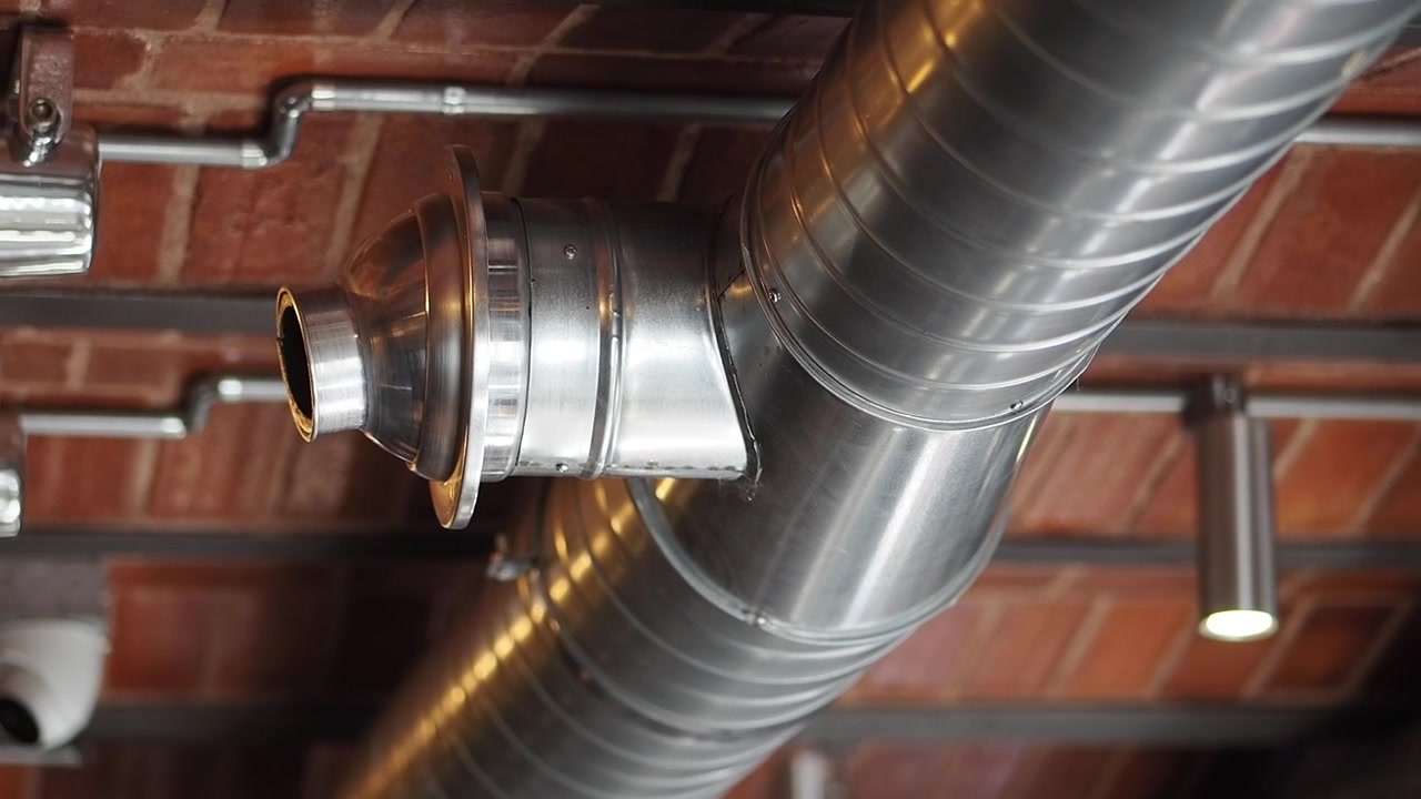 Industrielt ventilasjonssystem med synlige luftkanaler i metall og mursteinstak