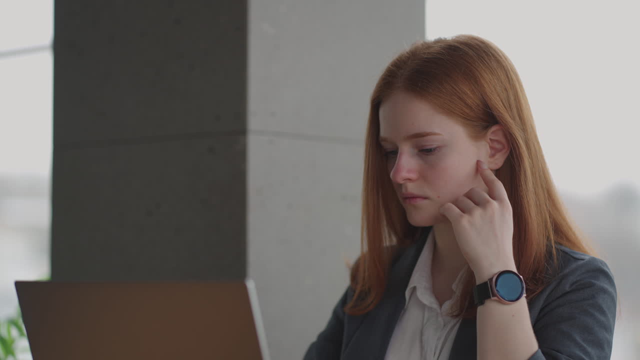 Thoughtful concerned redheaded woman working on laptop computer looking away thinking solving problem at office serious woman search for inspiration make decision feel lack of ideas
