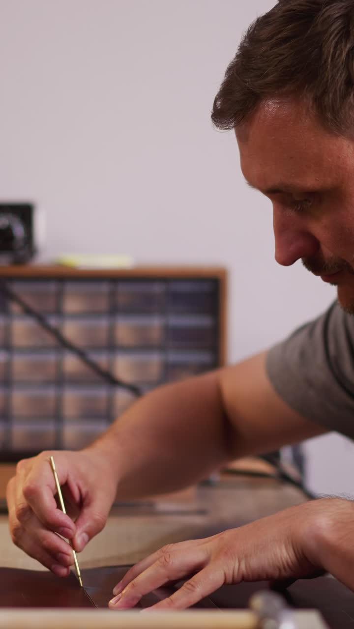 Concentrated man cuts natural leather sheet with small knife at workplace in workshop side view. Bearded master makes details of material for crafting