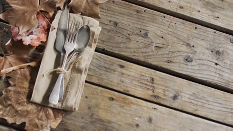 close up view of cutlery set over a napkin and autumn leaves with copy space on wooden surface