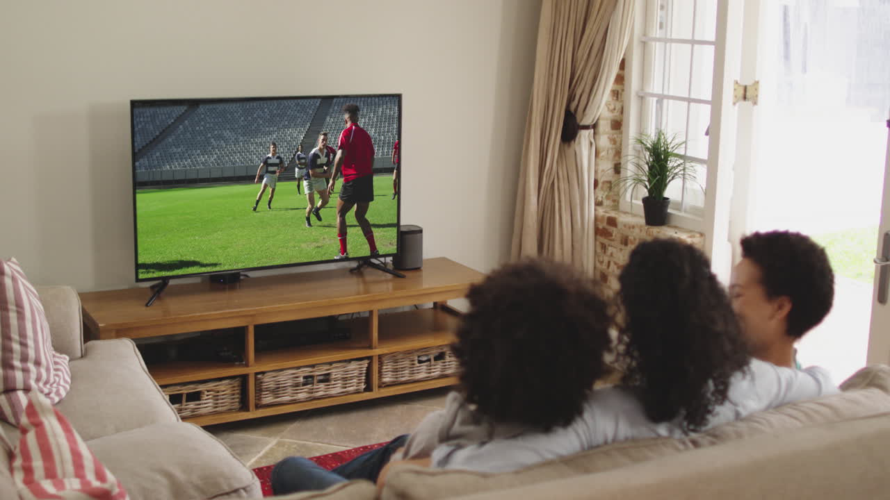 Famiglia felice seduta a casa insieme che guarda una partita di rugby in TV