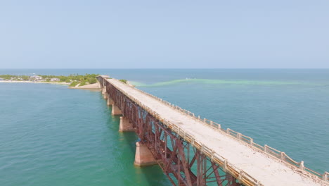 Aerial-pullback-along-sandy-broken-down-wooden-bridge-on-concrete-stilts-in-ocean