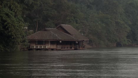 a distant shot of a thai house boat on the shore of the fast flowing khwae noi river in kanchanaburi, thailand