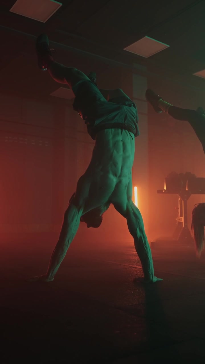 Uomo e donna atletici che eseguono verticali in una palestra buia con luci al neon