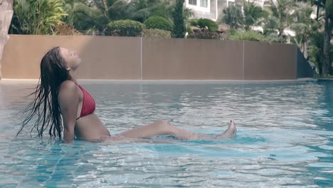 calm lady in red splashes water by legs in pool slow motion