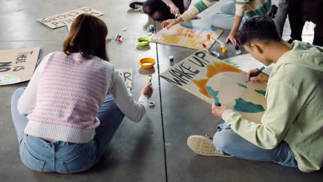 young environmental activists painting placards sitting on the floor