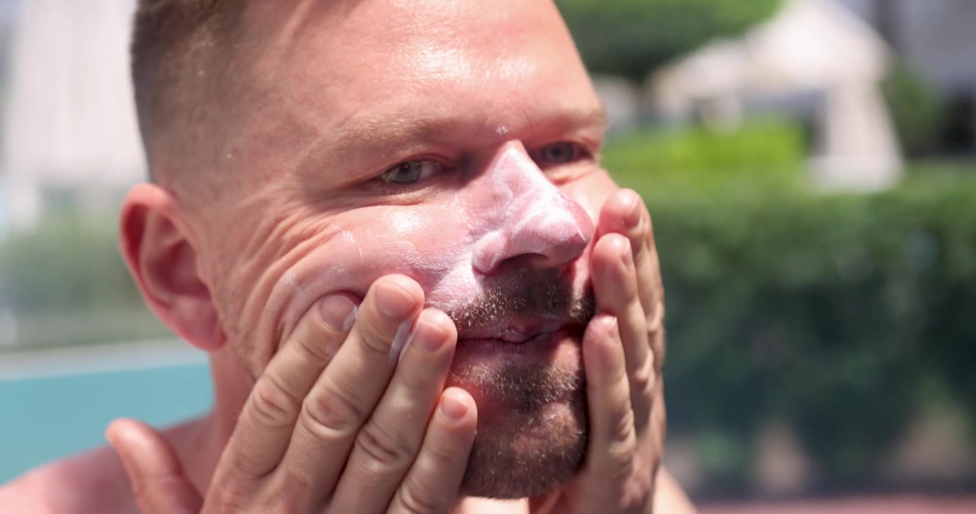 Ung mann smører ansiktet med solkrem på stranden, 4k-film