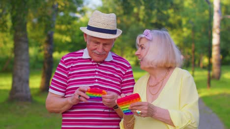 stylish senior grandmother grandfather playing squeezing anti-stress toy simple dimple game in park