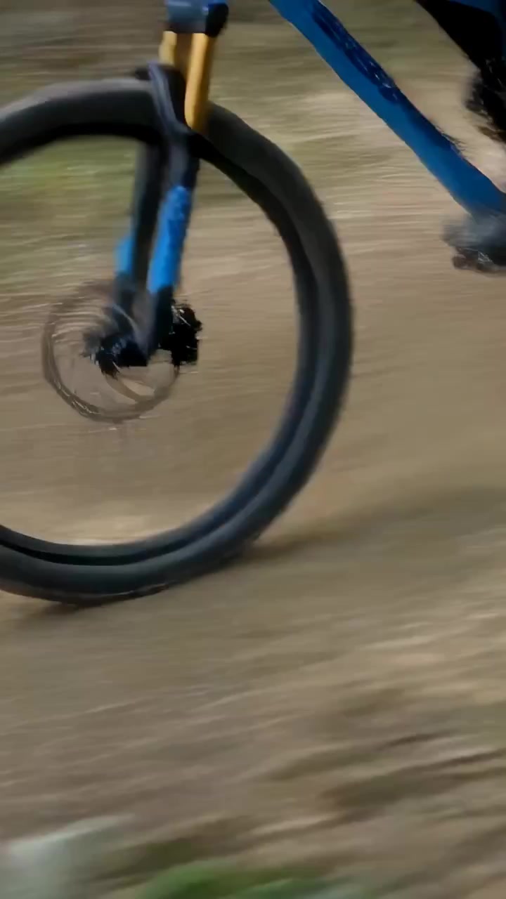 Video verticale: Ciclista con scarpe scure che pedala energicamente su una bici blu lungo un sentiero polveroso, con la ruota sfocata.