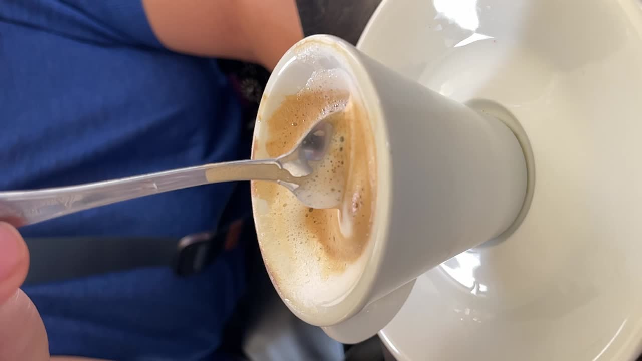 Close up vertical video shot an espresso coffee foam stirred with a metal spoon