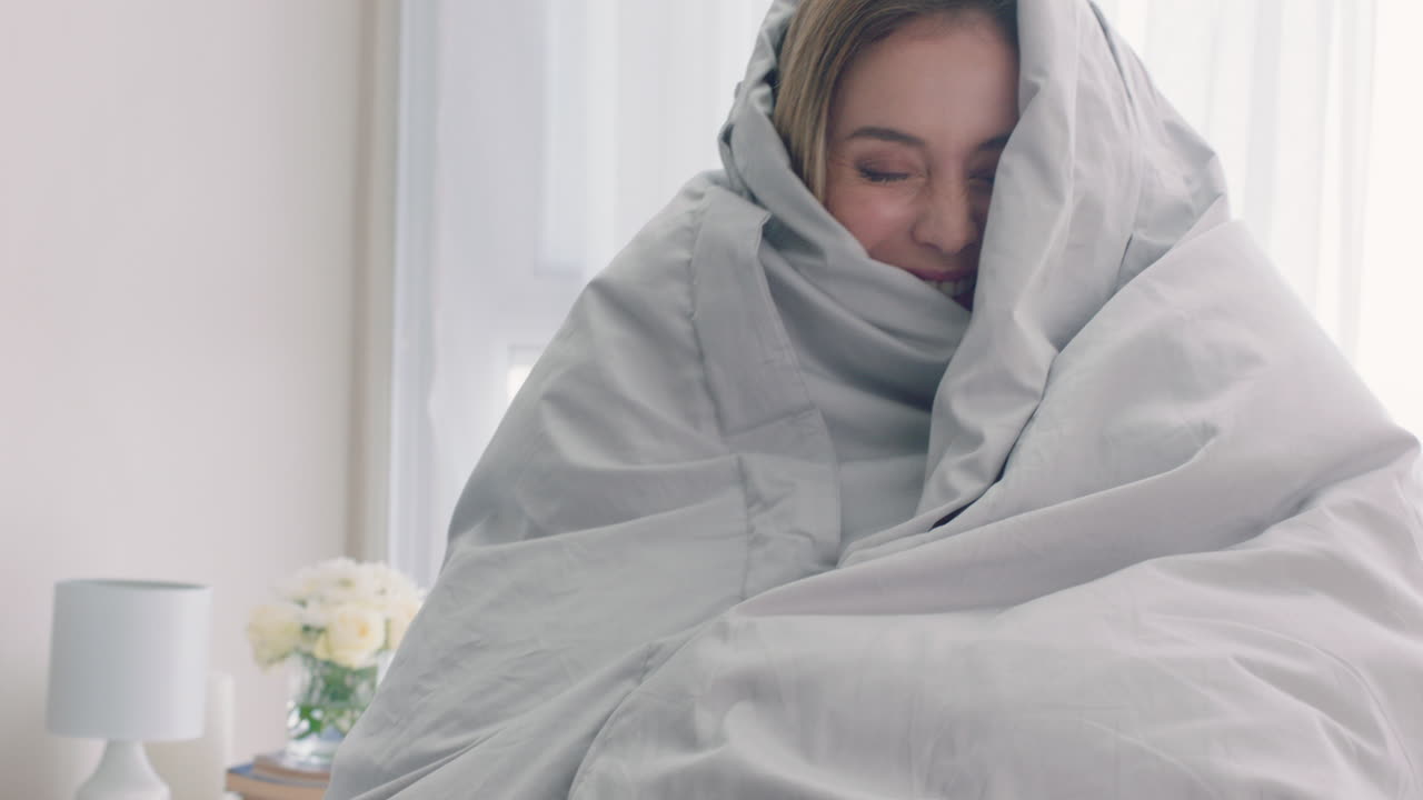 침대에서 놀고 있는 아름다운 여성이 담요  ⁇ 에 숨어서 집에서 즐거운 아침을 즐기고 있습니다.