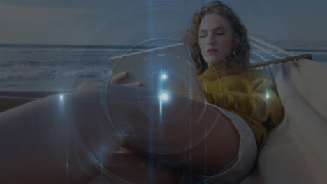 animación de un haz de luz con un círculo sobre una mujer caucásica usando una tableta digital en una hamaca en la playa