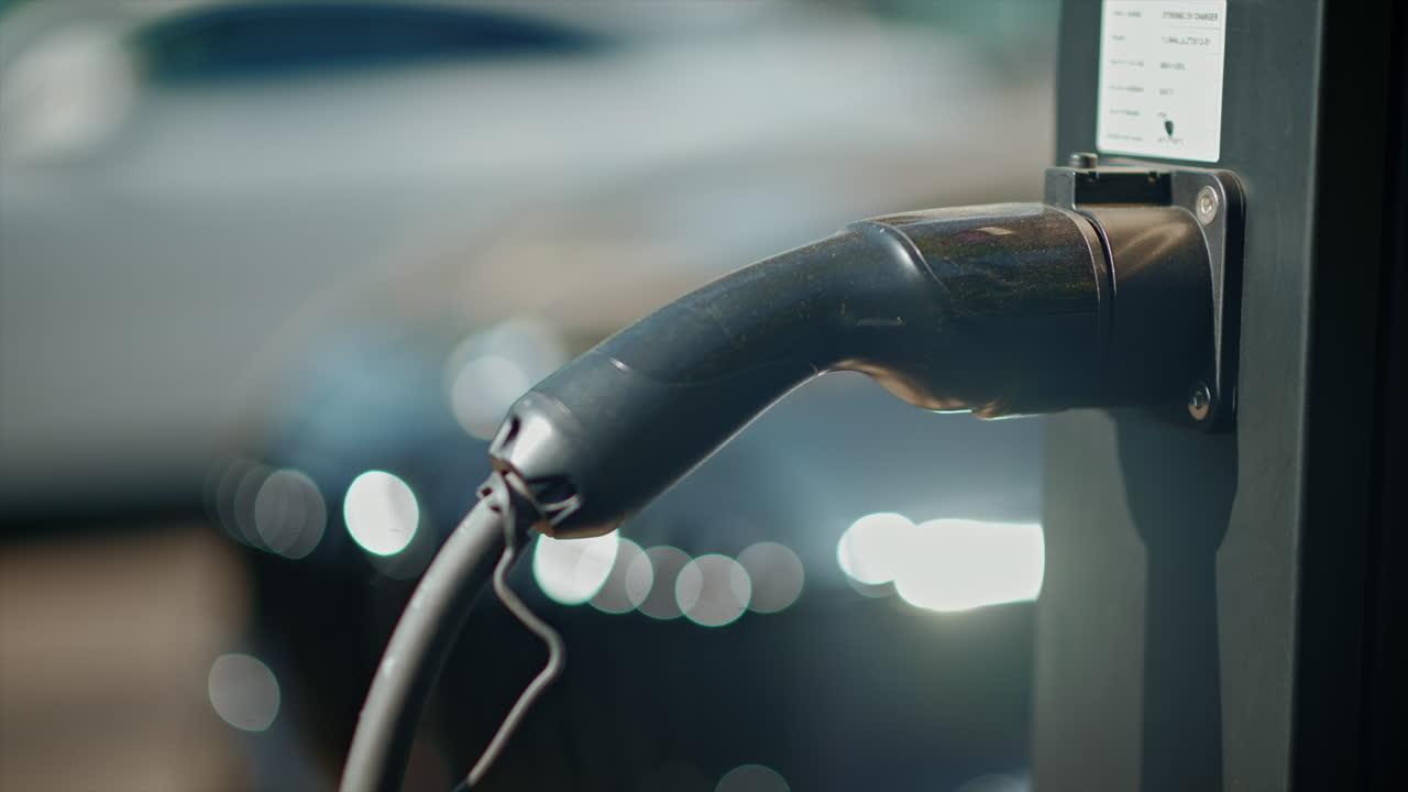 Close-up of electric car charging station with a white car on the background