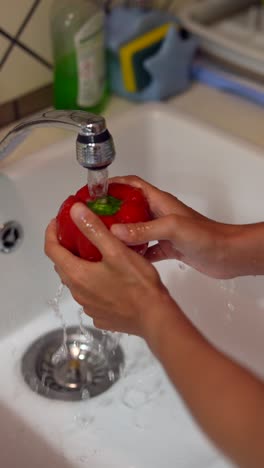 washing a red bell pepper in the kitchen sink