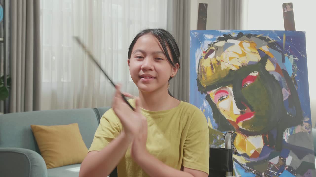 Asian Artist Girl In Wheelchair Holding Paintbrush Wipe The Sweat Before Crossing His Arms And Smiling After Finish Painting On The Canvas