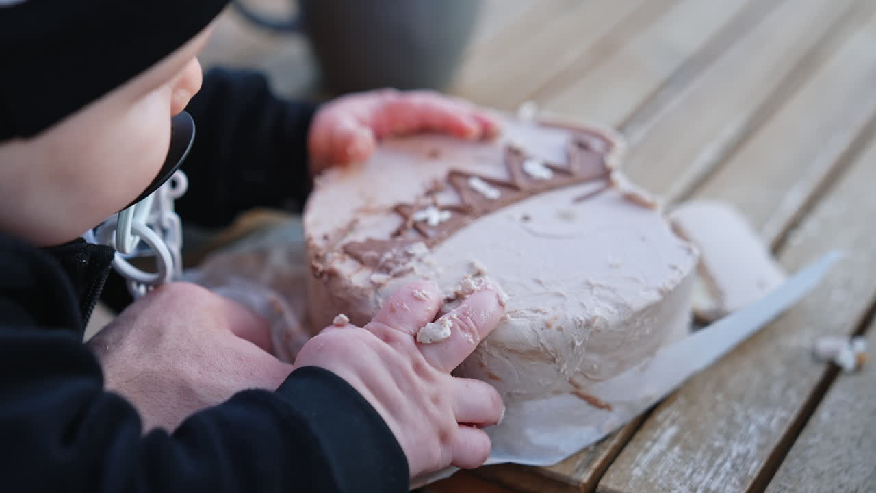 Unrecognized infant trying to grab a cake in front of him. Baby with pacifier takes the cream from dessert. Close up.