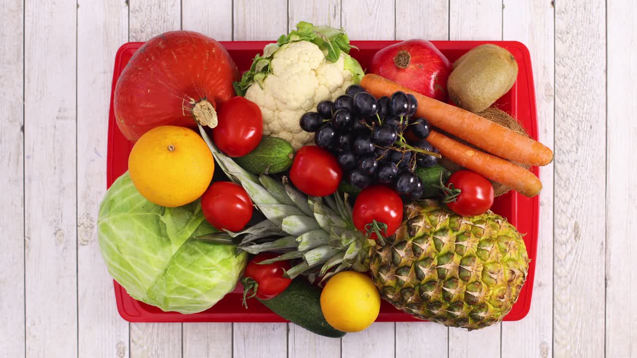 Organic vegetables and fruits appear in red tray on wooden theme. Stop motion