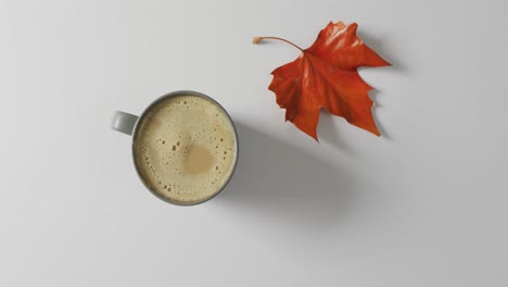 video of top view of mug with coffee and fall leaf on white background