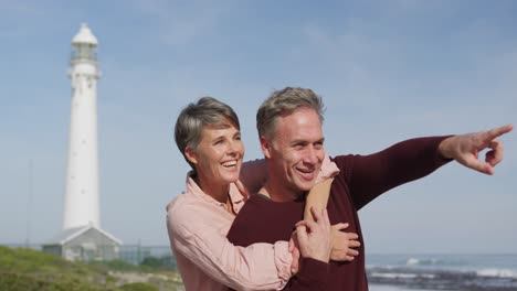 Caucasian-couple-enjoying-free-time-by-sea-on-sunny-day-pointing-finger