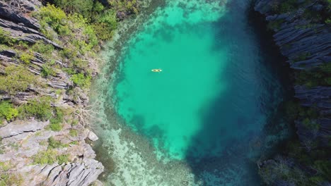 4k drone video looking down from a birds eye view of a couple kayaking around green lagoon near coron in palawan, philippines