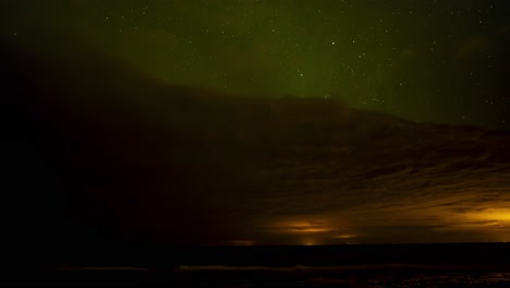 beautiful time lapse of green northern lights above dark clouds with a starry night sky with shooting stars