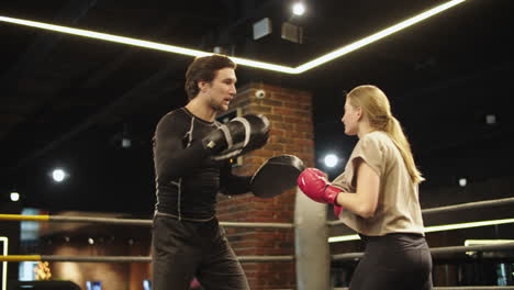 Serious-male-boxer-instructing-female-boxer-on-boxing-ring.-Sport-couple-at-gym