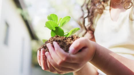 Madre-E-Hija-De-Raza-Mixta-Cultivando-Un-Huerto-En-Un-Jardín-Soleado,-Cuidando-Las-Plantas