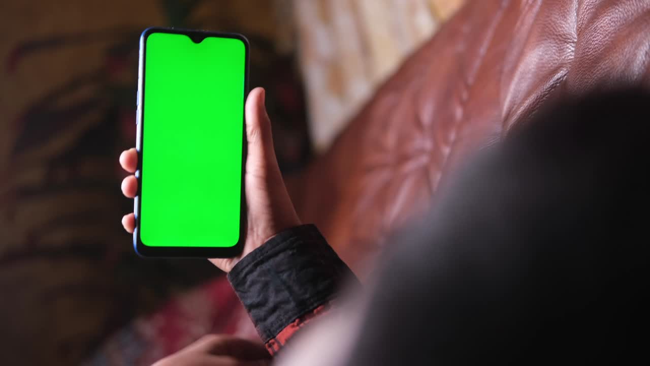 hombres jóvenes sosteniendo un teléfono inteligente con pantalla verde tendido en el sofá